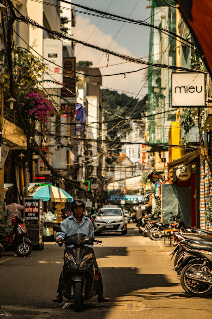A man on a scooter in a Saigon side street under tangled power lines
